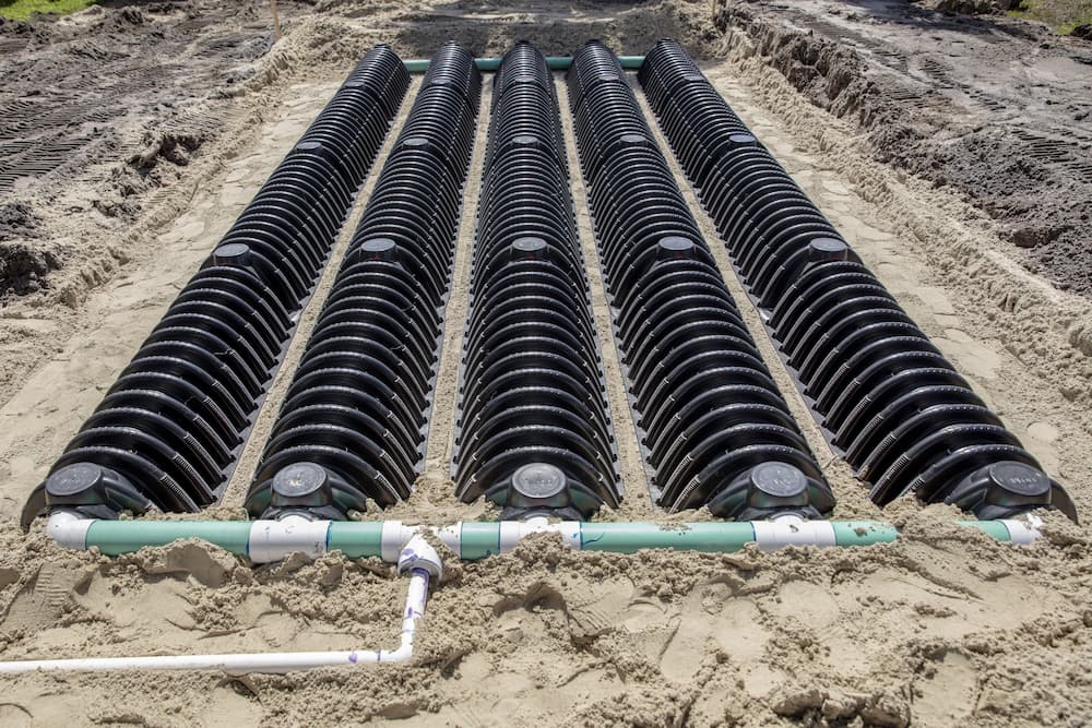 New leach field installation with rows of infiltrator chambers and green distribution pipes in sand
